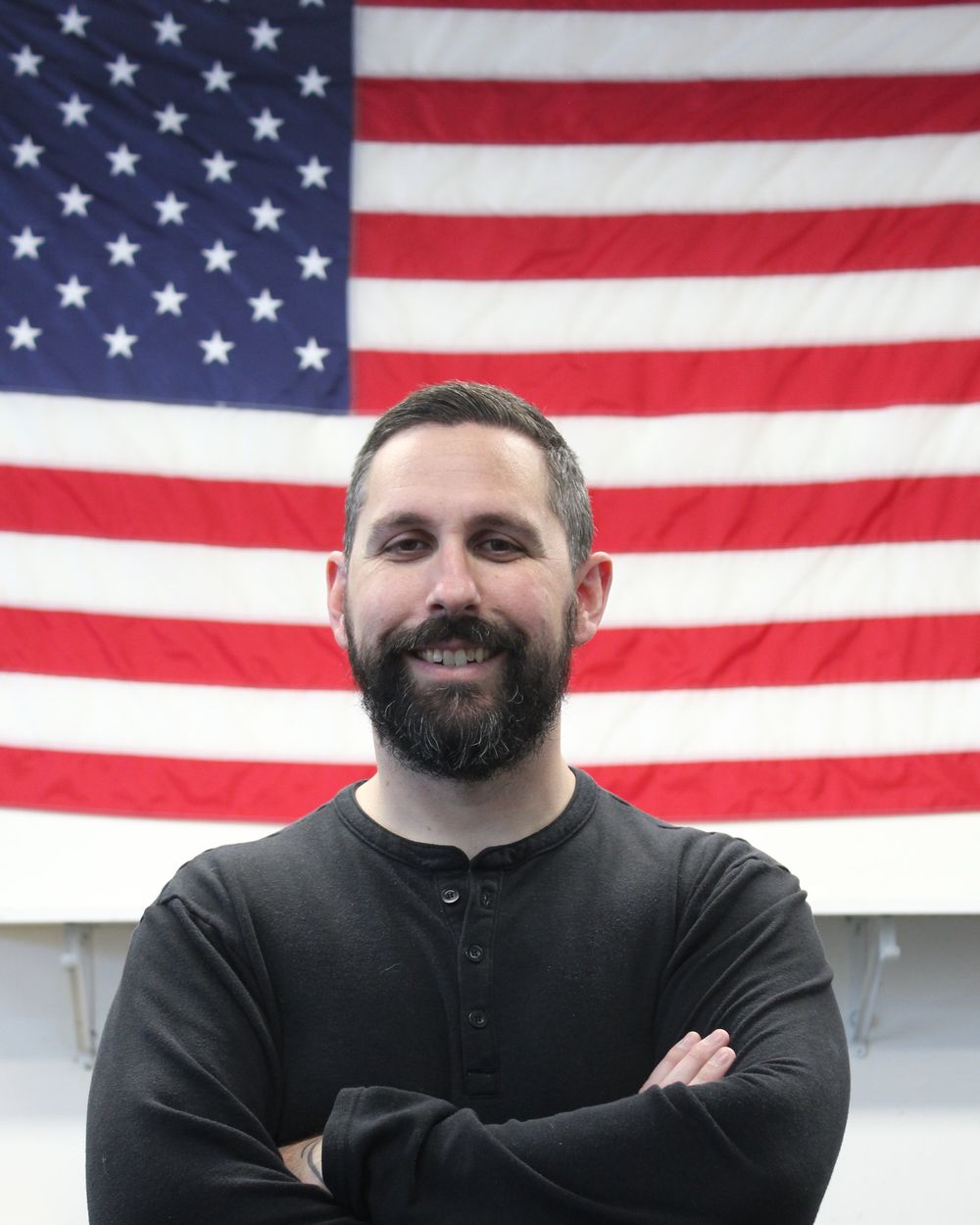 Alex Van Drie, owner of Titan Works Manufacturing, standing in front of an American flag in the shop