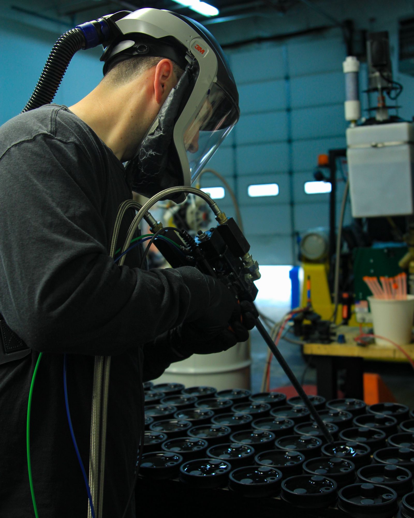 Technician in a supplied-air respirator filling a tray of bump stop molds from a two-part polyurethane dispensing gun